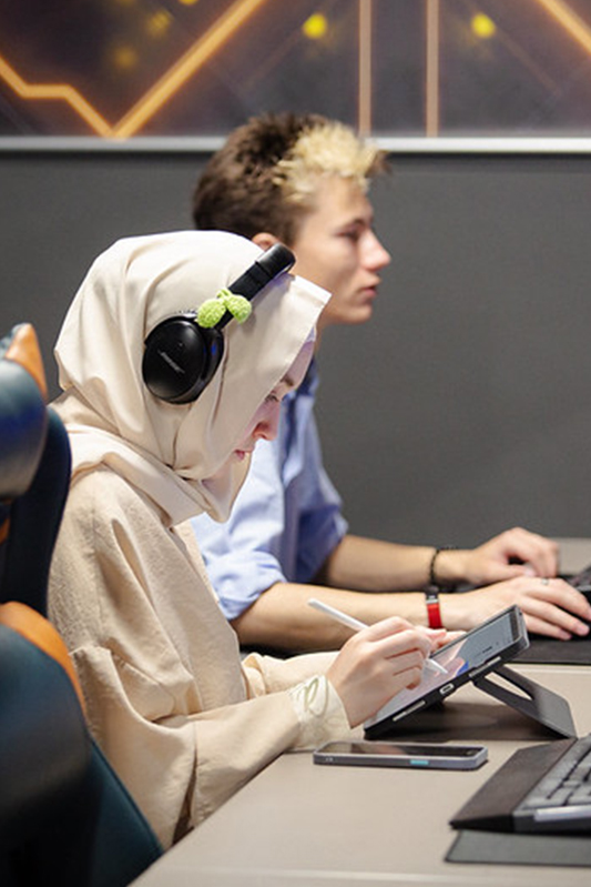 Students studying Games Art and Animation. A student is facing down towards a digital drawing tablet, deep in concentration.