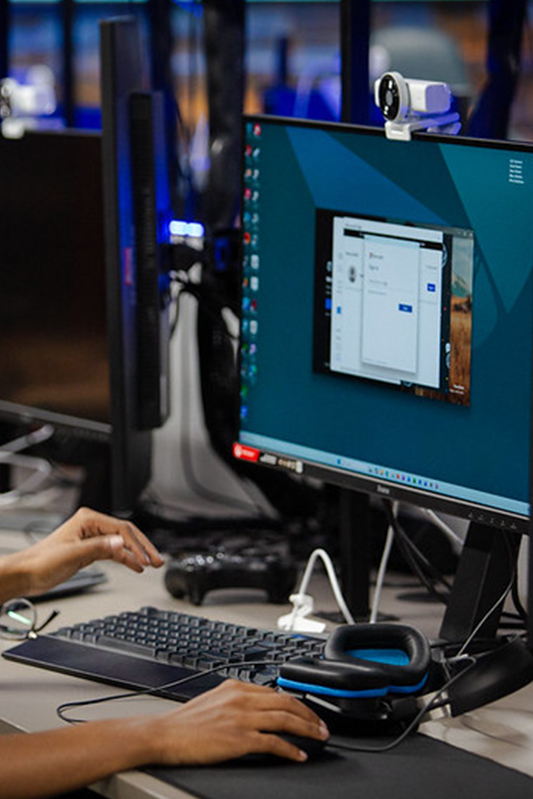Students studying Games Design and Development. A student is sat facing a PC monitor in a vibrant gaming room.